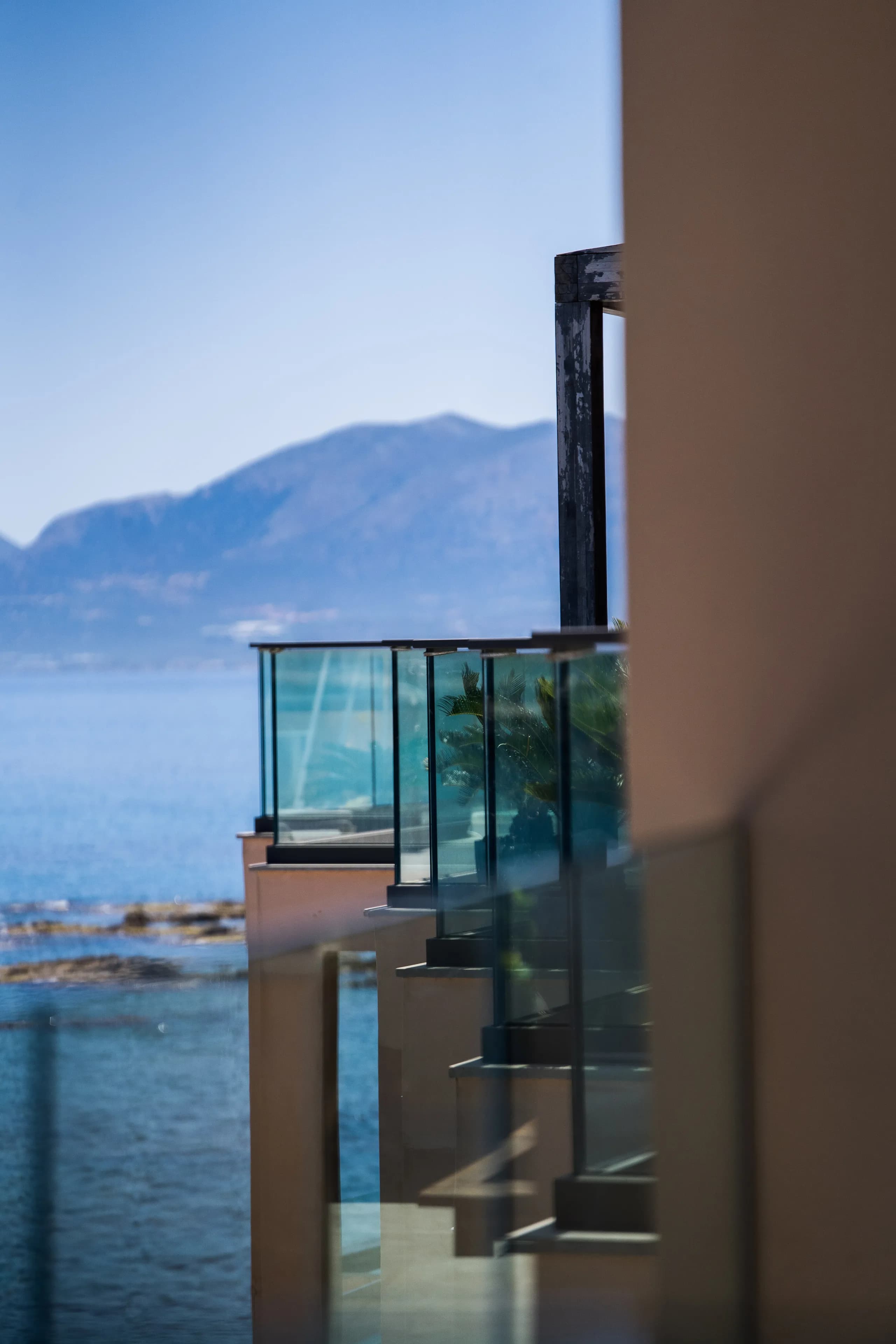 Glass balconies of a seaside building, with the sea and mountains behind