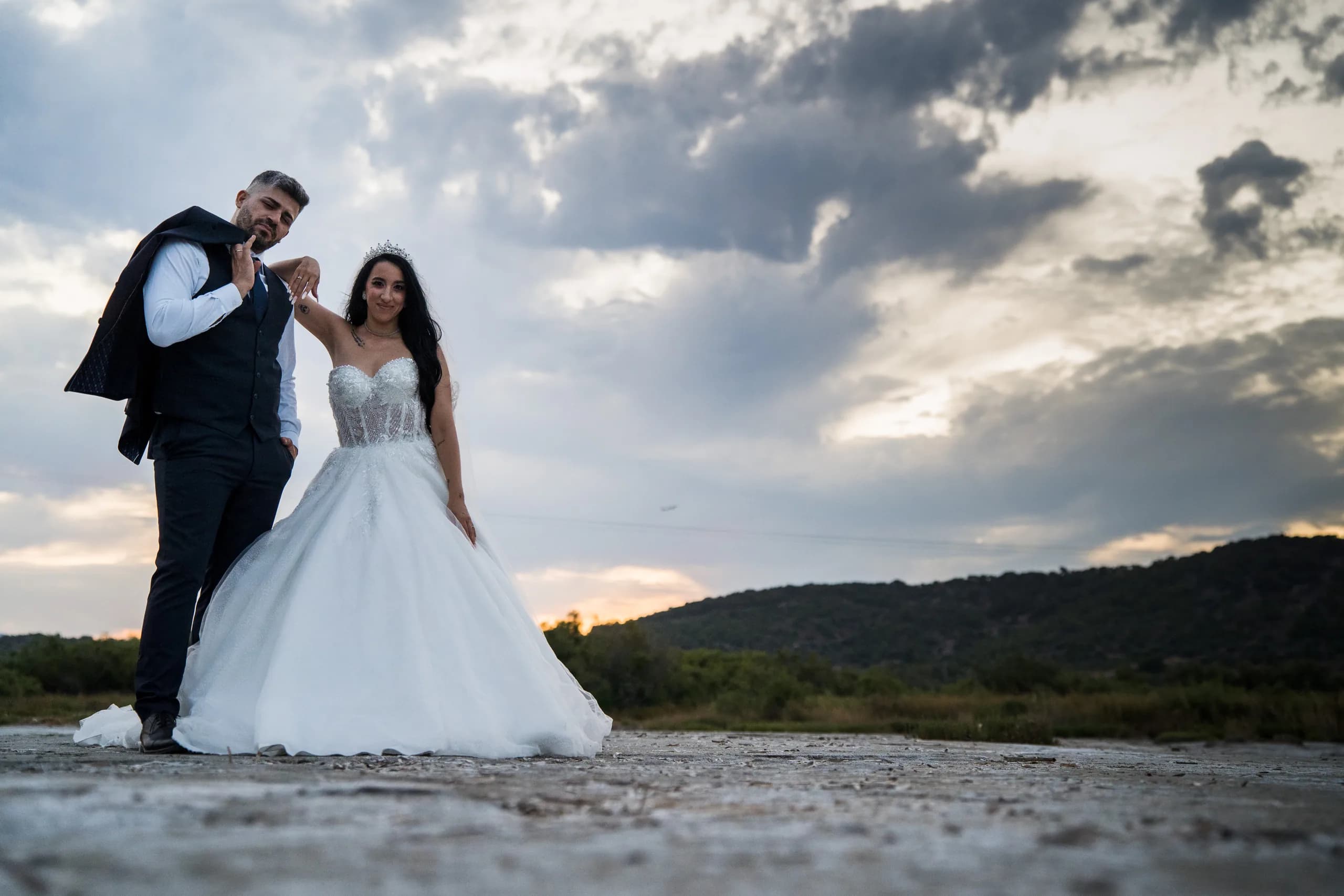 Το ζευγάρι σε μια ακτή κάτω από δραματικό συννεφιασμένο ουρανό, με το σακάκι του γαμπρού στον ώμο
