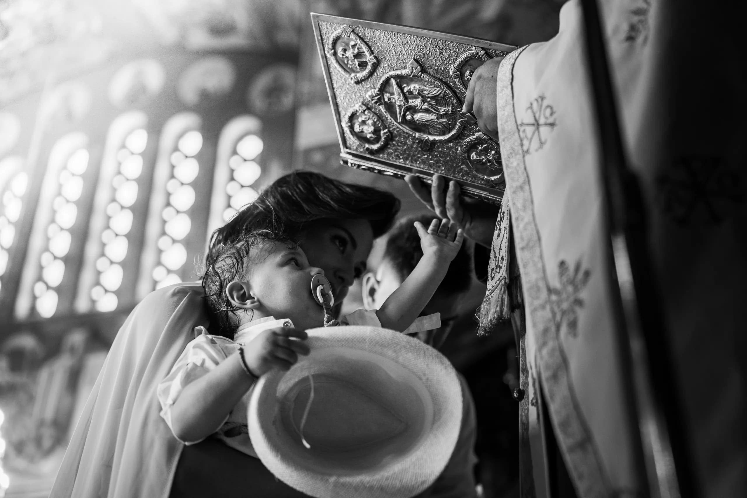 Baby in a woman's arms reaching up to the Gospel book held by the priest