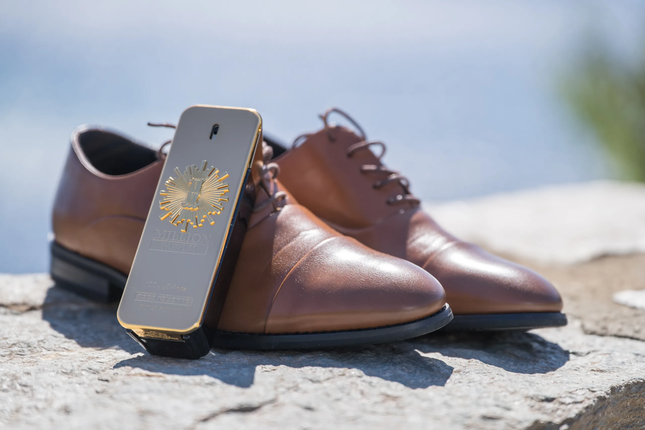 The groom's brown shoes and a bottle of cologne on a sunlit stone ledge