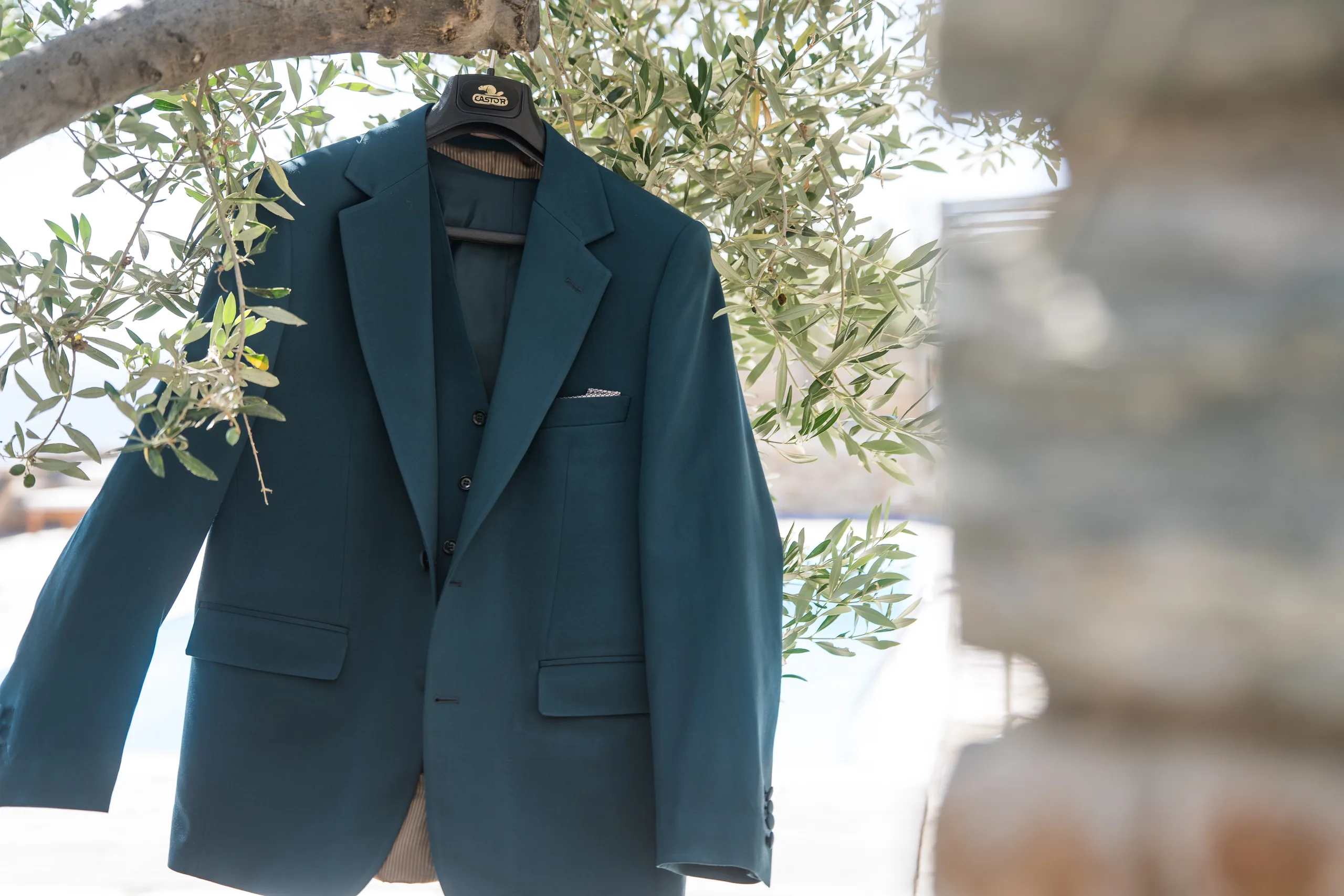 The groom's teal jacket hanging from an olive tree