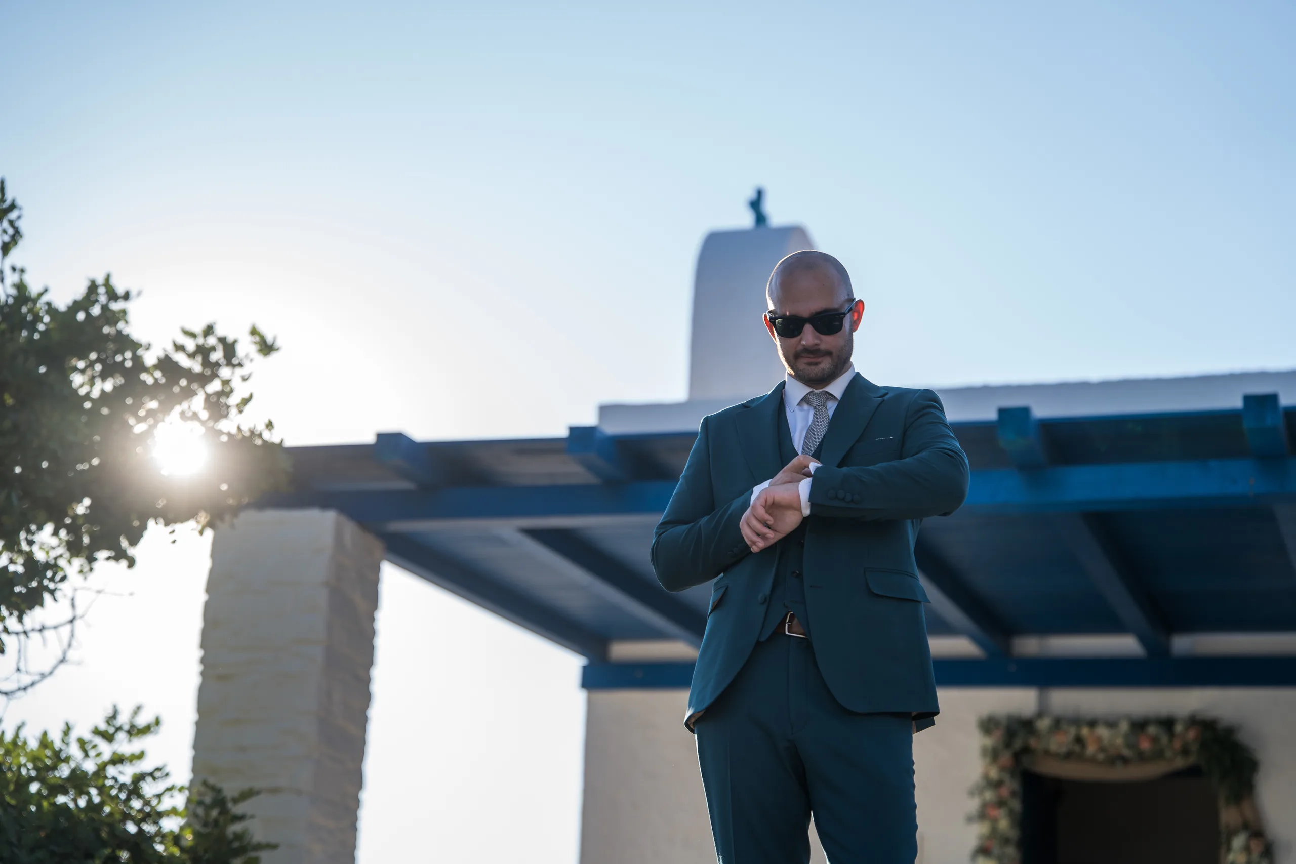 The groom in sunglasses checking his watch outside a whitewashed chapel