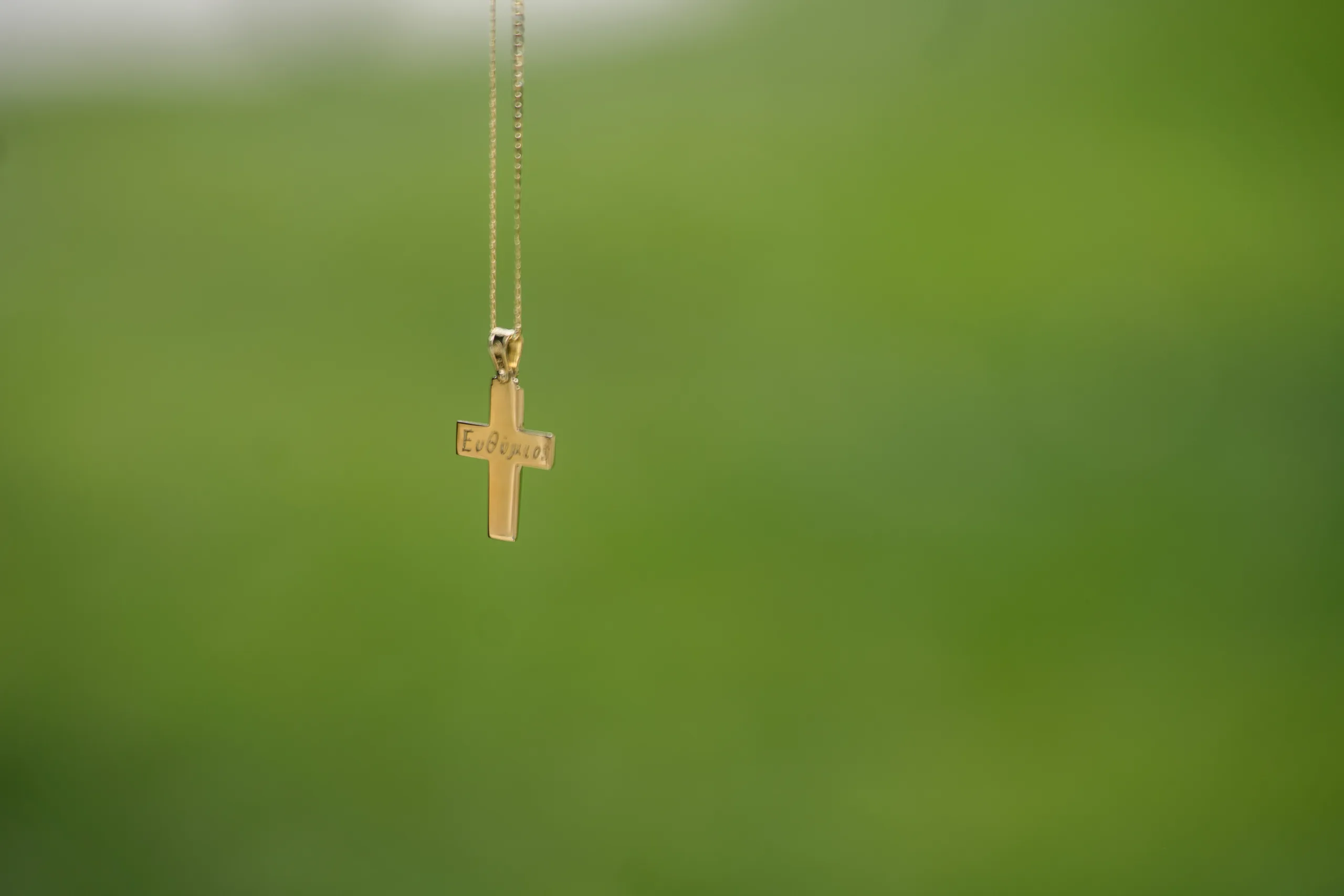 A gold cross on a chain against green leaves