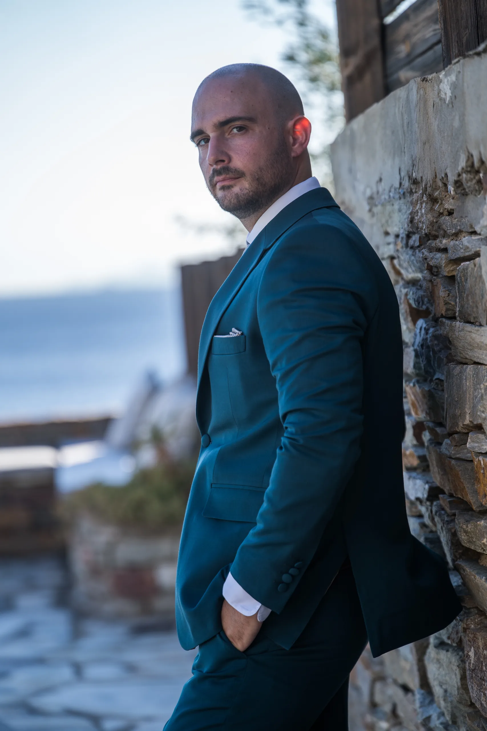 The groom in his teal suit leaning on a stone wall