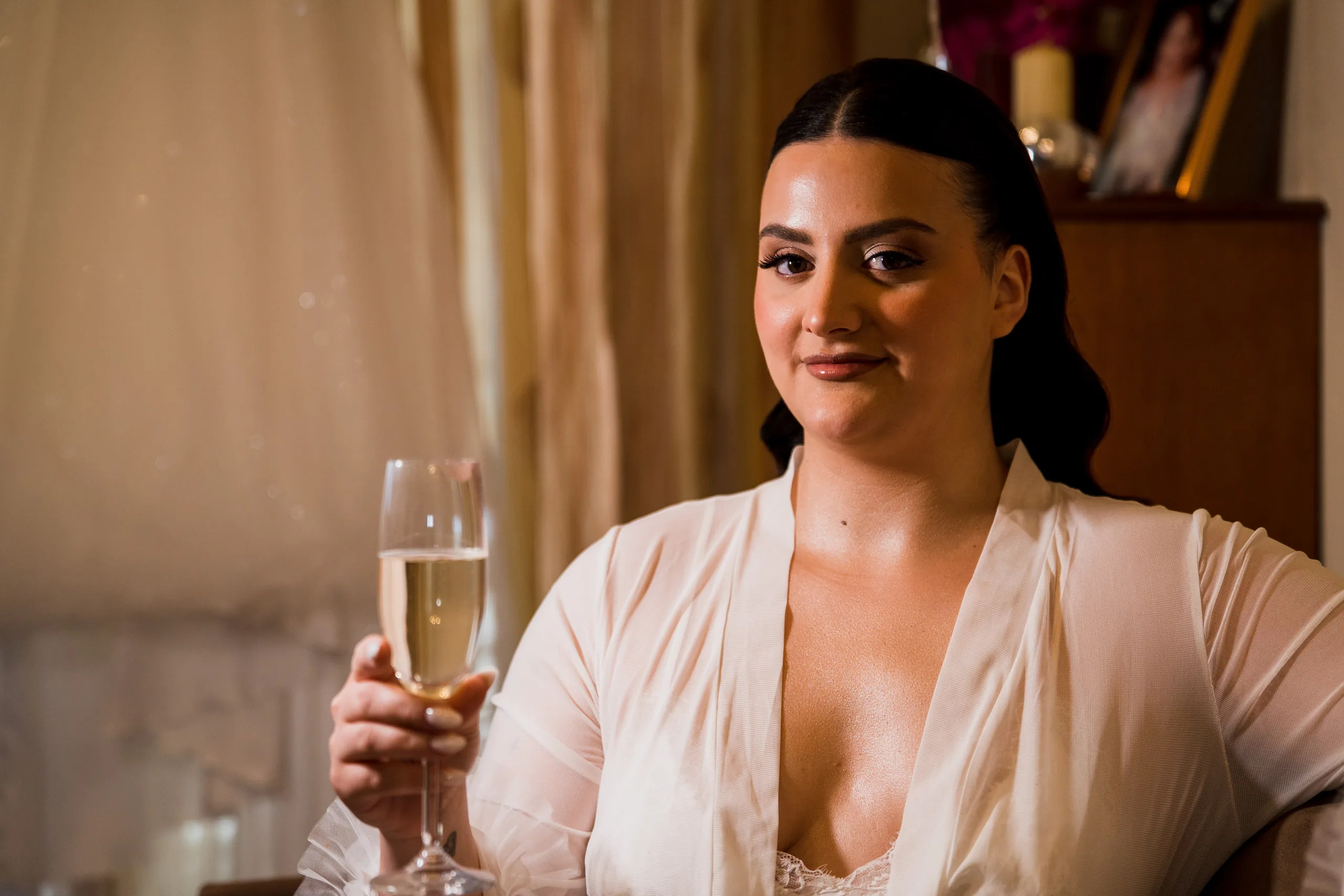The bride in a white robe holding a glass of champagne