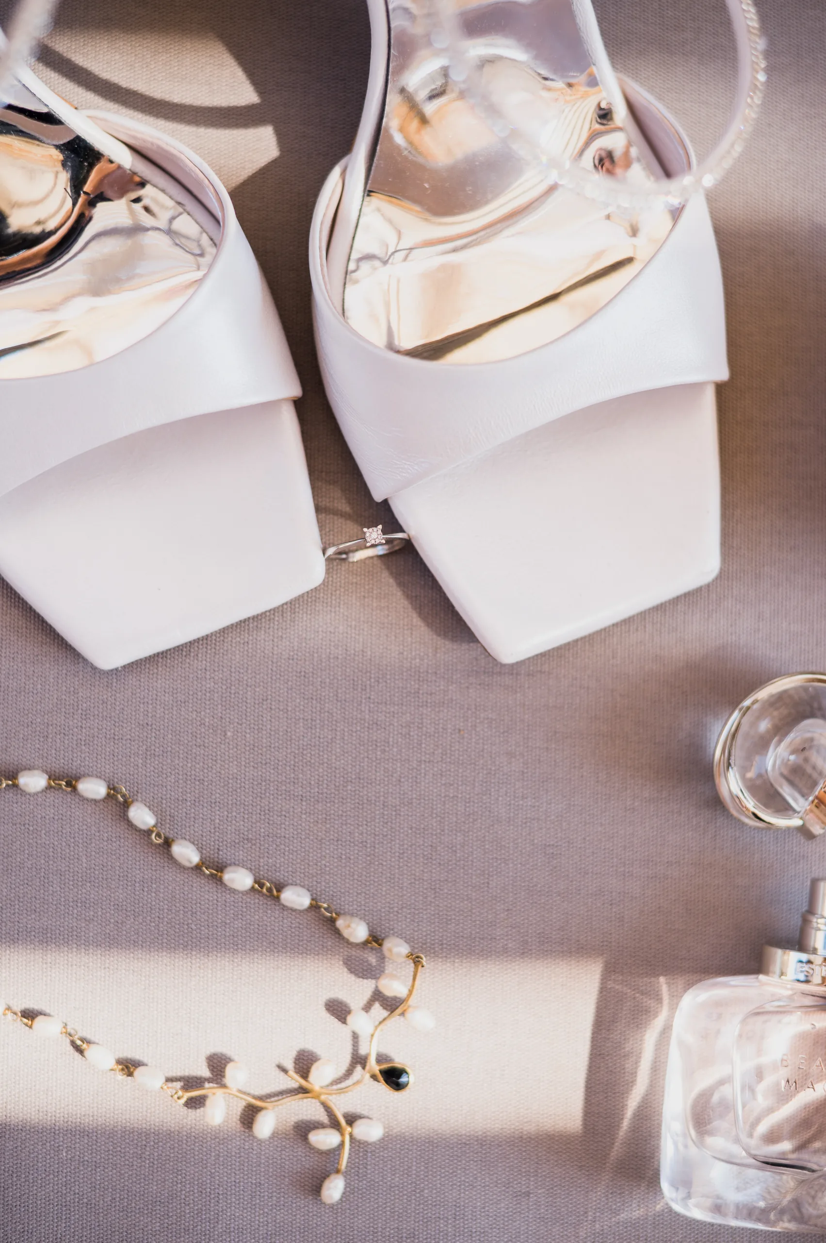 The bride's white sandals, ring, pearl necklace and perfume