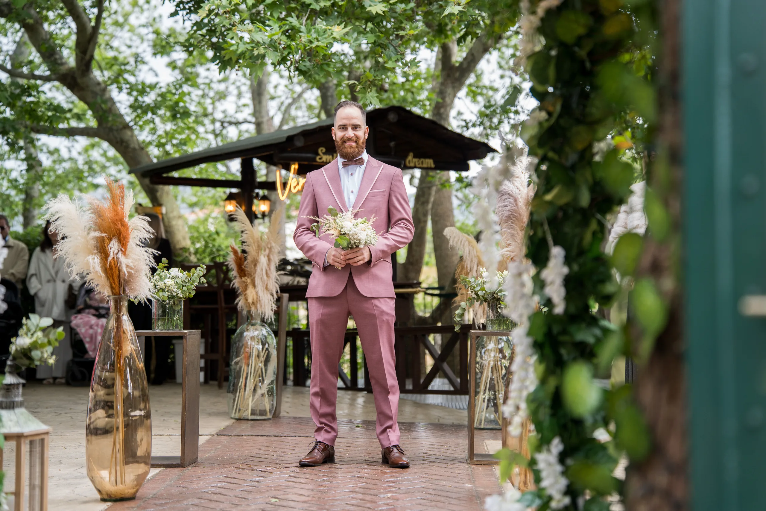 The groom smiling at the end of the aisle in a garden