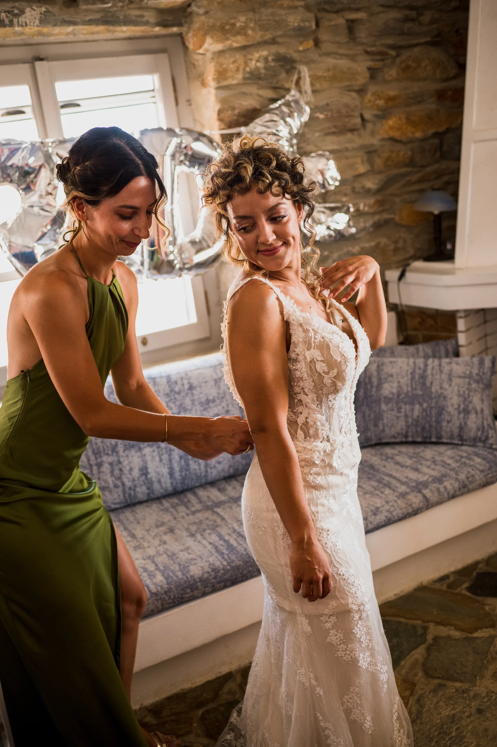 A bridesmaid in green helps the bride into her dress