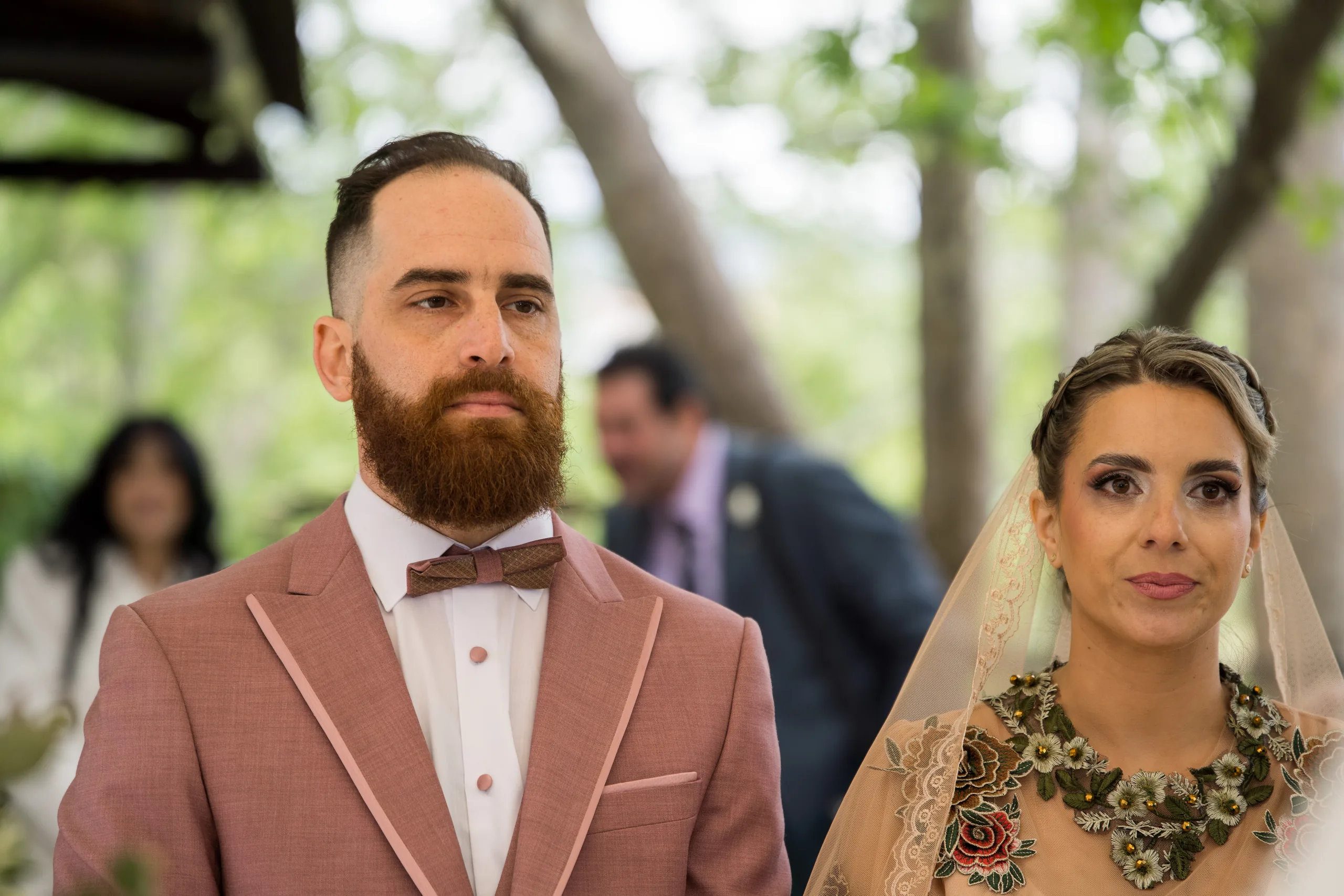 The groom in a pink suit and the bride in her veil at the ceremony