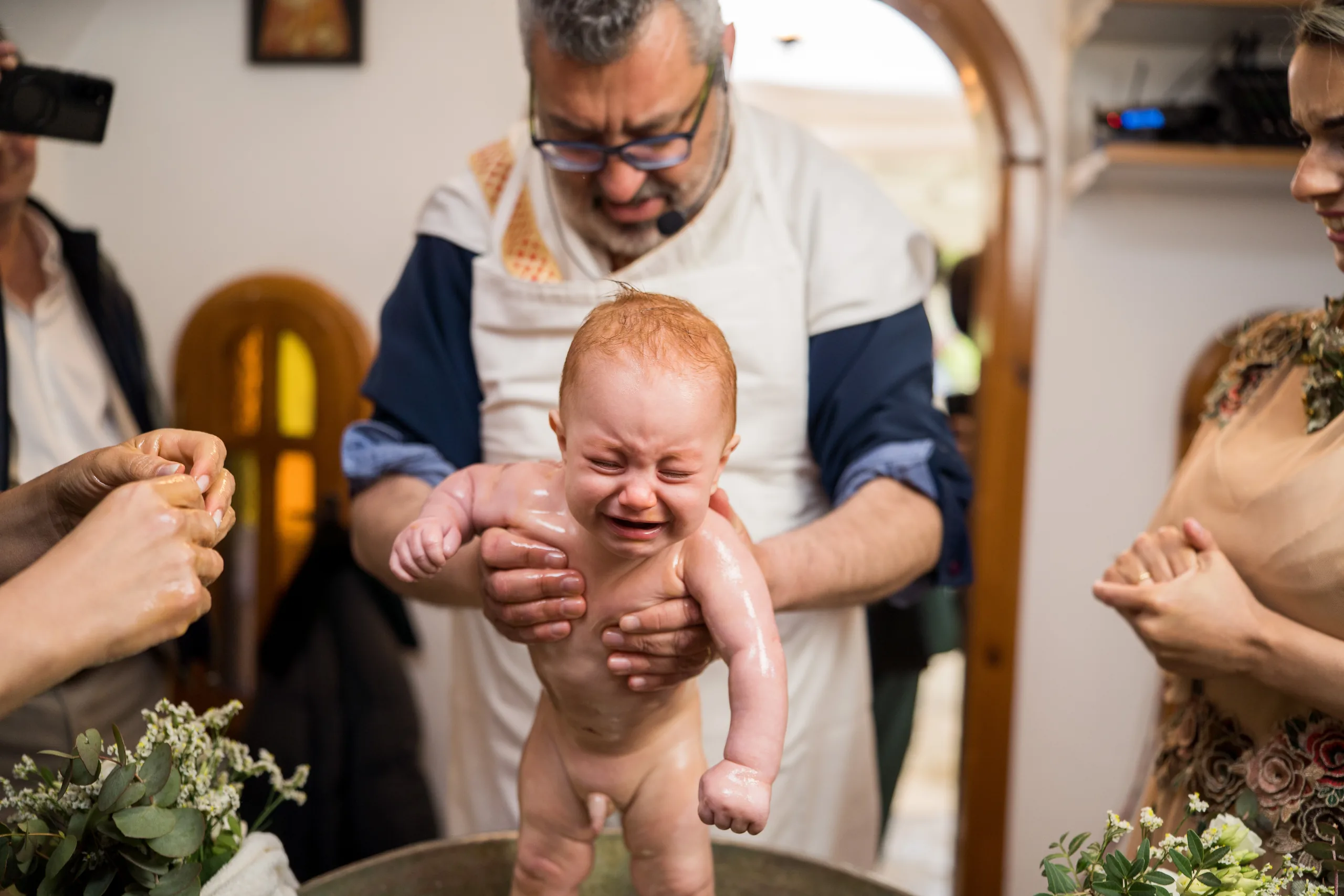 The priest holds the crying baby at the baptism