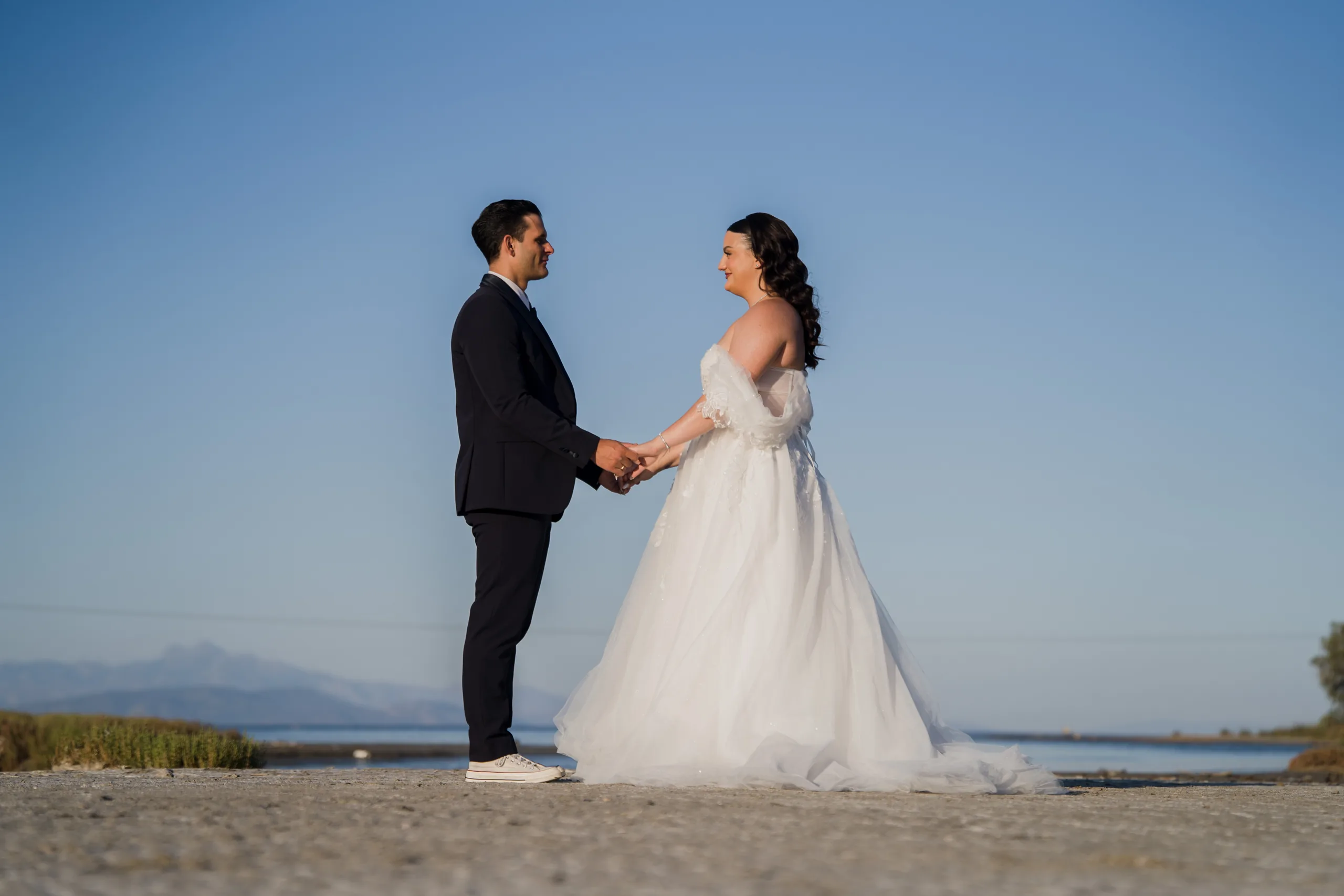 The couple holding hands by the sea under a blue sky