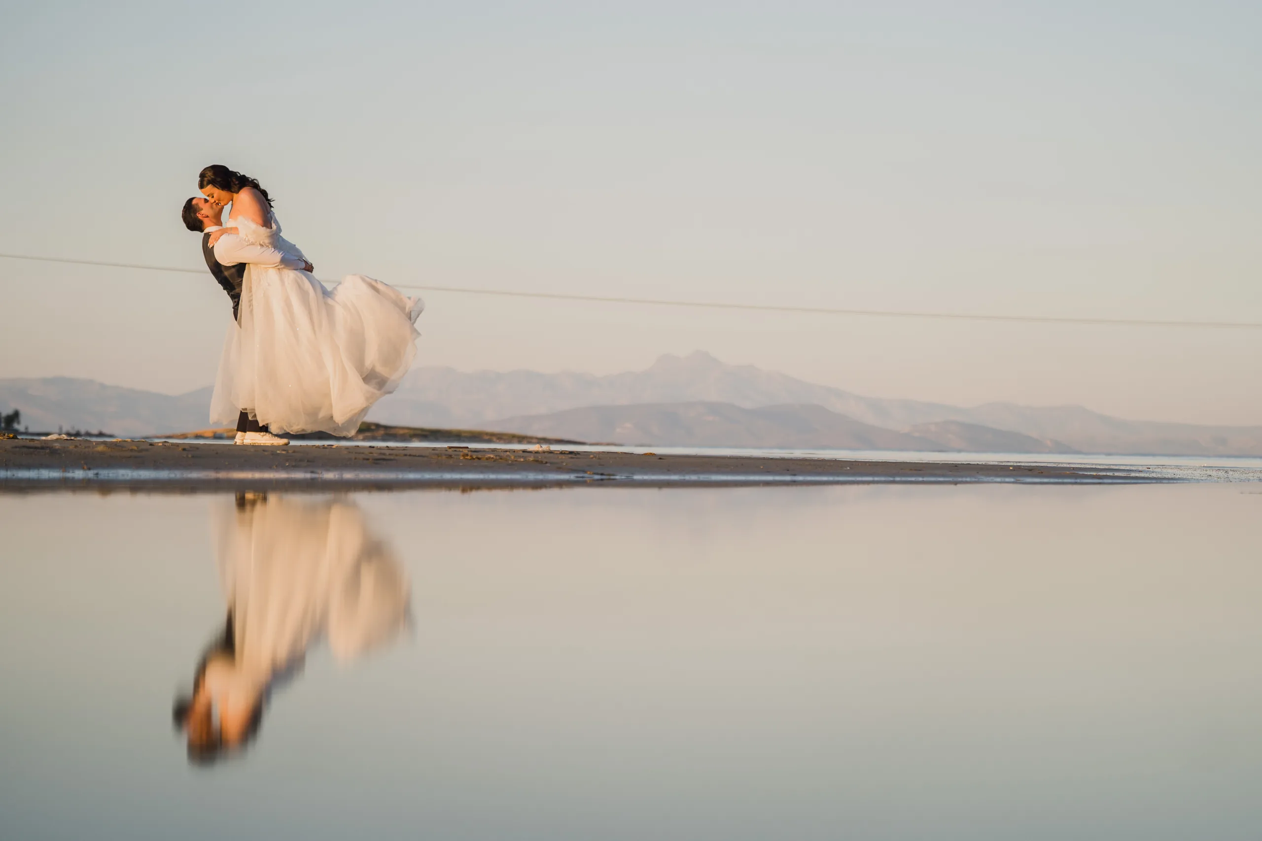 The groom lifts the bride, mirrored in still water