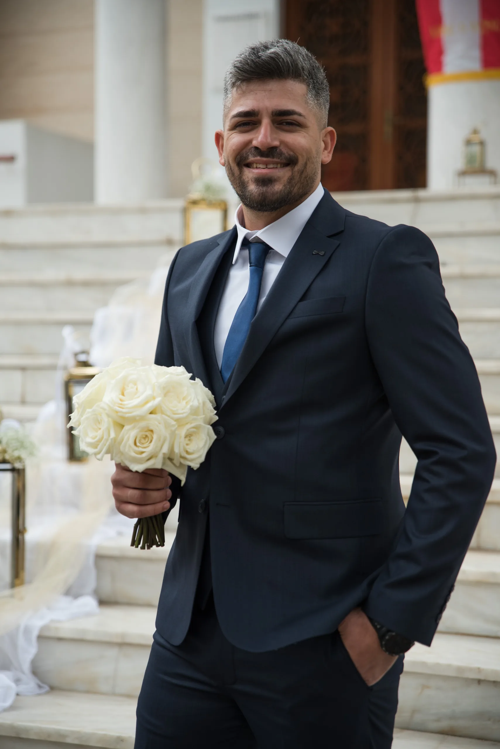 Ο γαμπρός κρατά λευκά τριαντάφυλλα στα σκαλιά της εκκλησίας