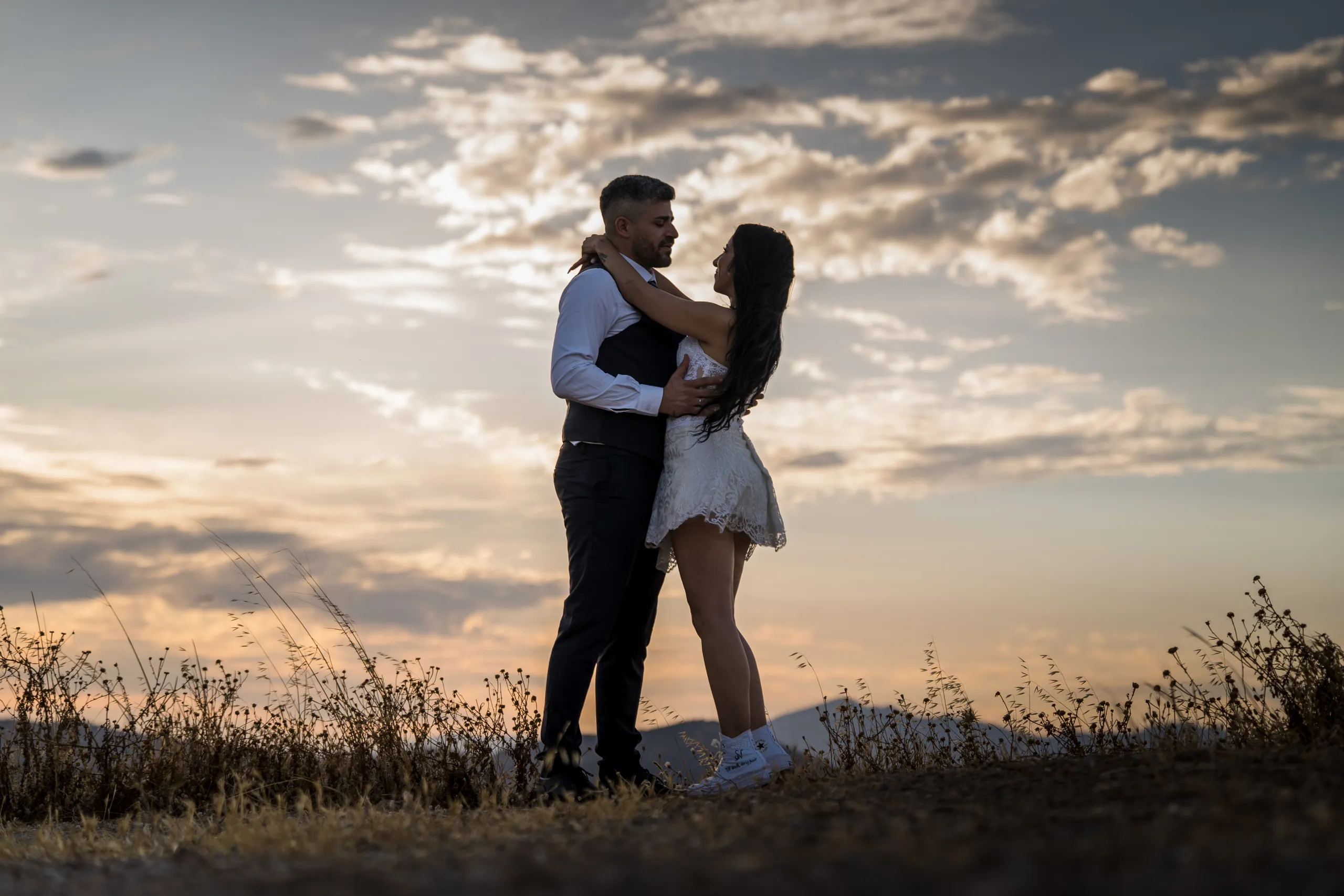 Bride and groom embracing on a hilltop against a sunset sky