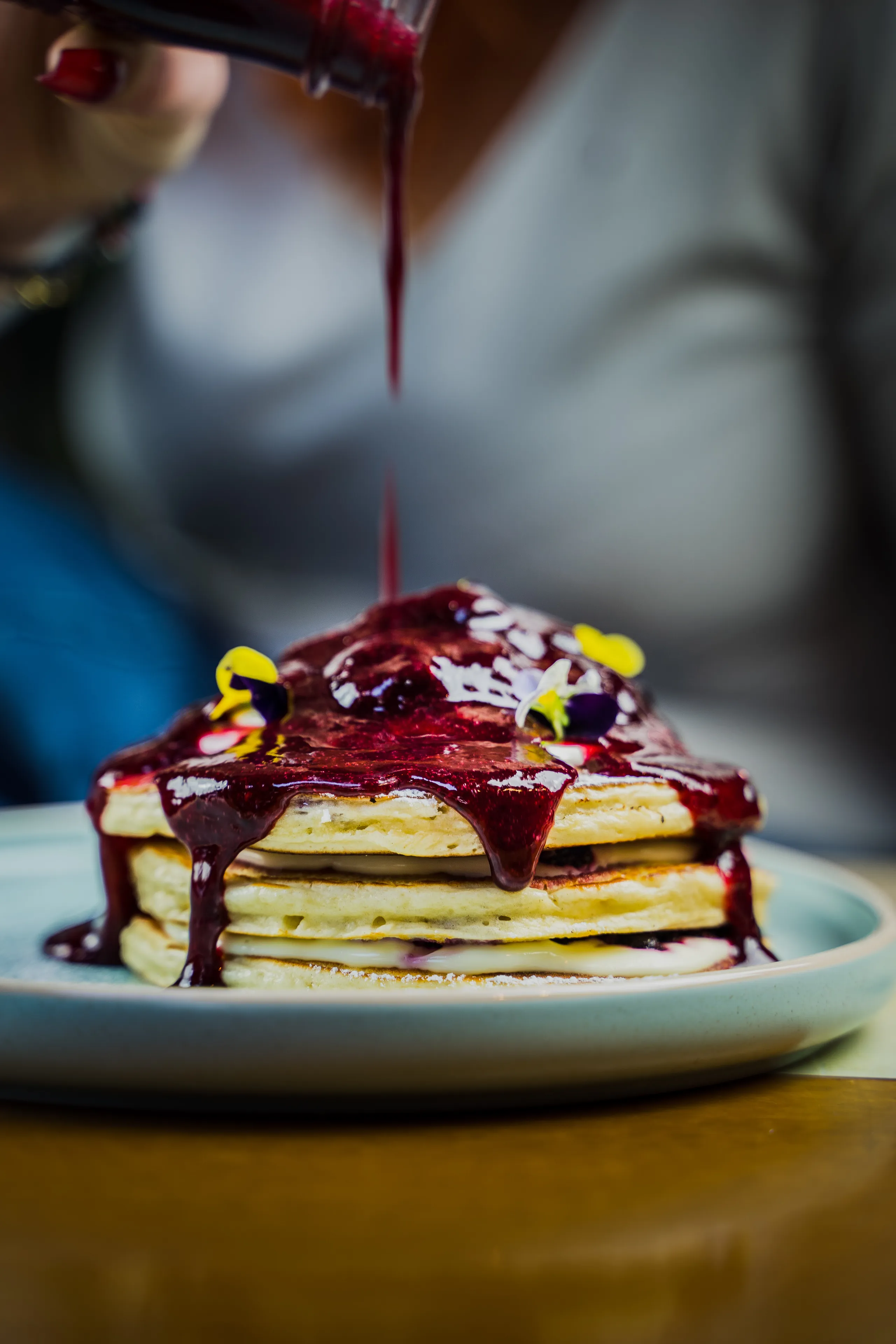 Berry sauce poured over a stack of pancakes topped with edible flowers