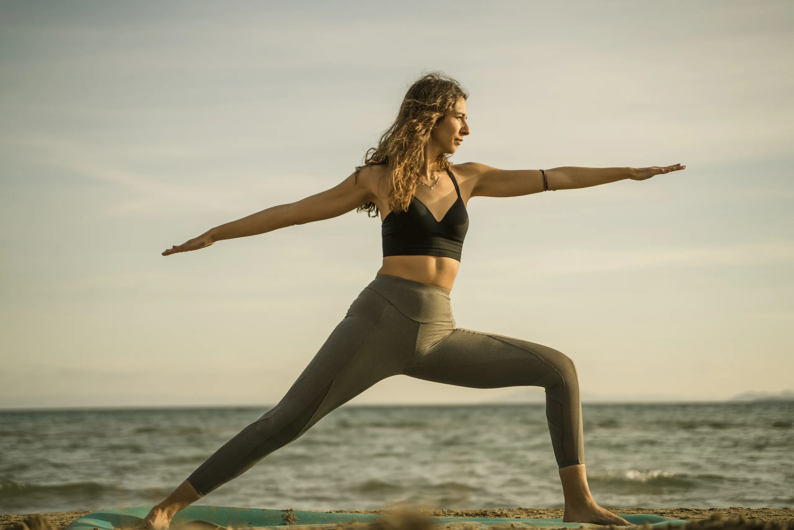 Woman in a warrior yoga pose by the sea