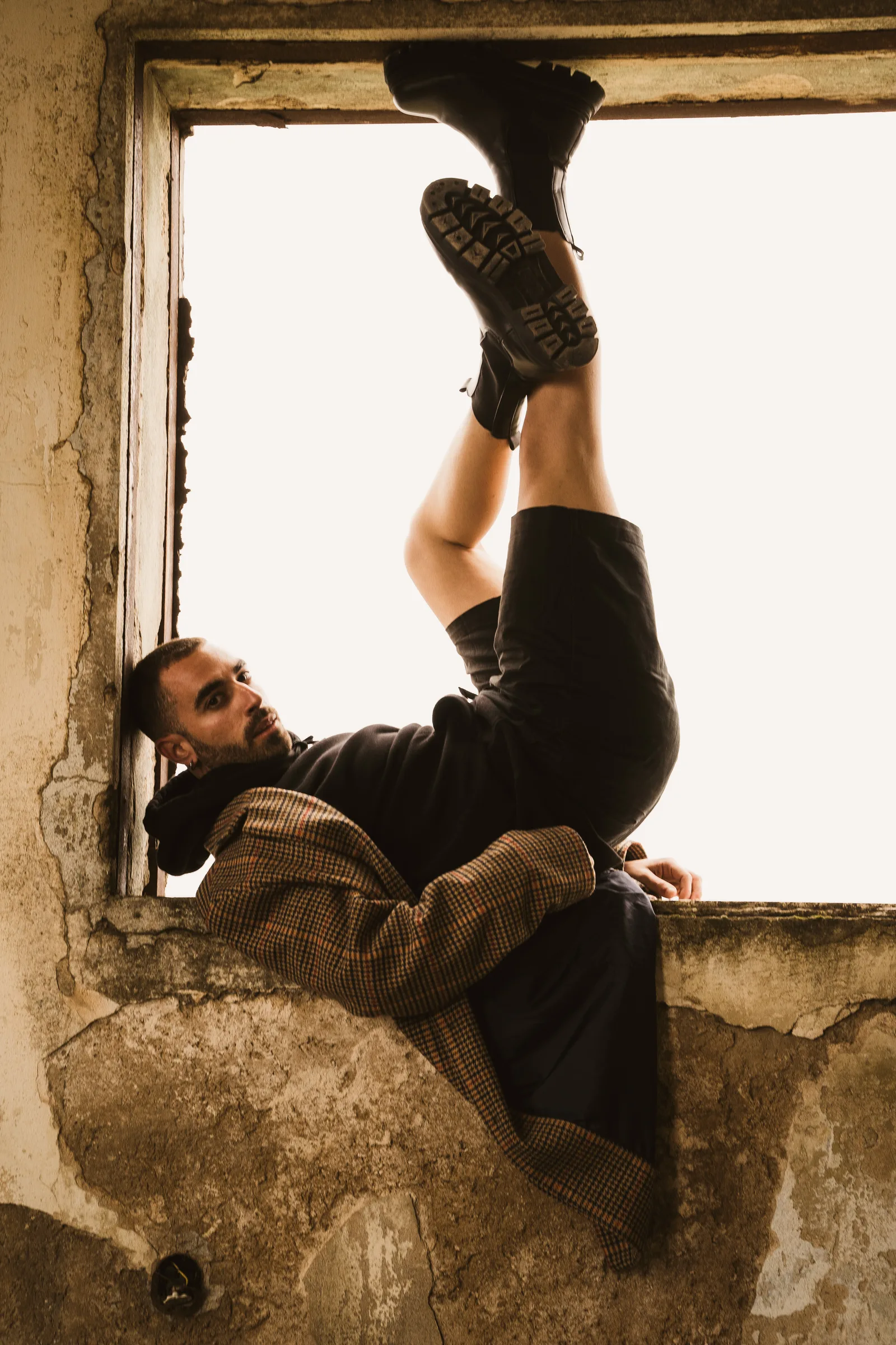 Model lying back on a ruined window ledge, boots in the air