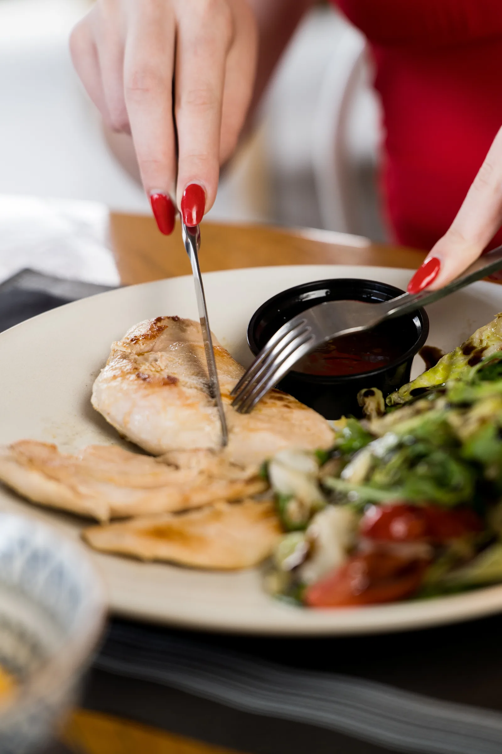 Diner cutting into grilled chicken with a side salad